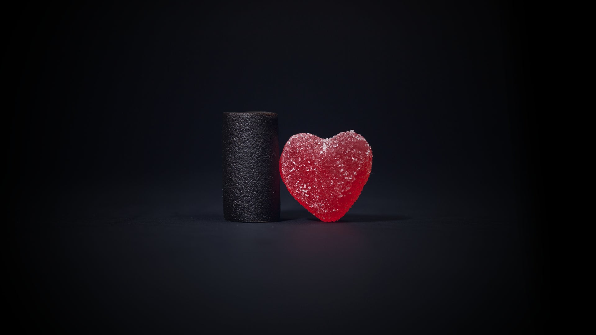 Kuva, jossa tummalla taustalla on lakupala sekä punainen sydämen muotoinen marmeladi. 