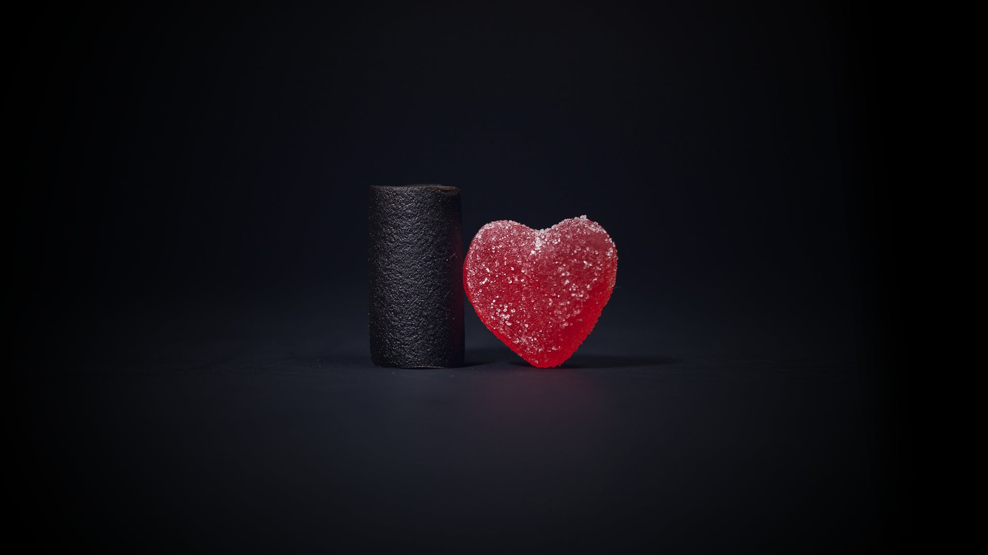 Kuva, jossa tummalla taustalla on lakupala sekä punainen sydämen muotoinen marmeladi.